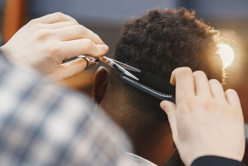 Close-up of a professional barber trimming an afro hairstyle with scissors and comb.