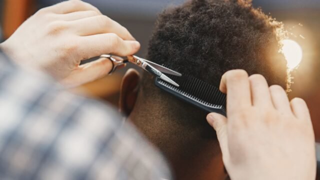 Close-up of a professional barber trimming an afro hairstyle with scissors and comb.
